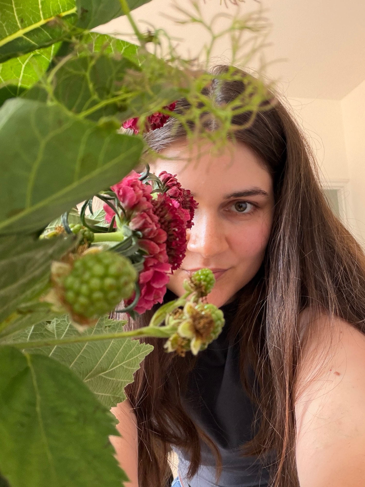 Woman with dark hair peeking through magenta flowers and green foliage toward the camera