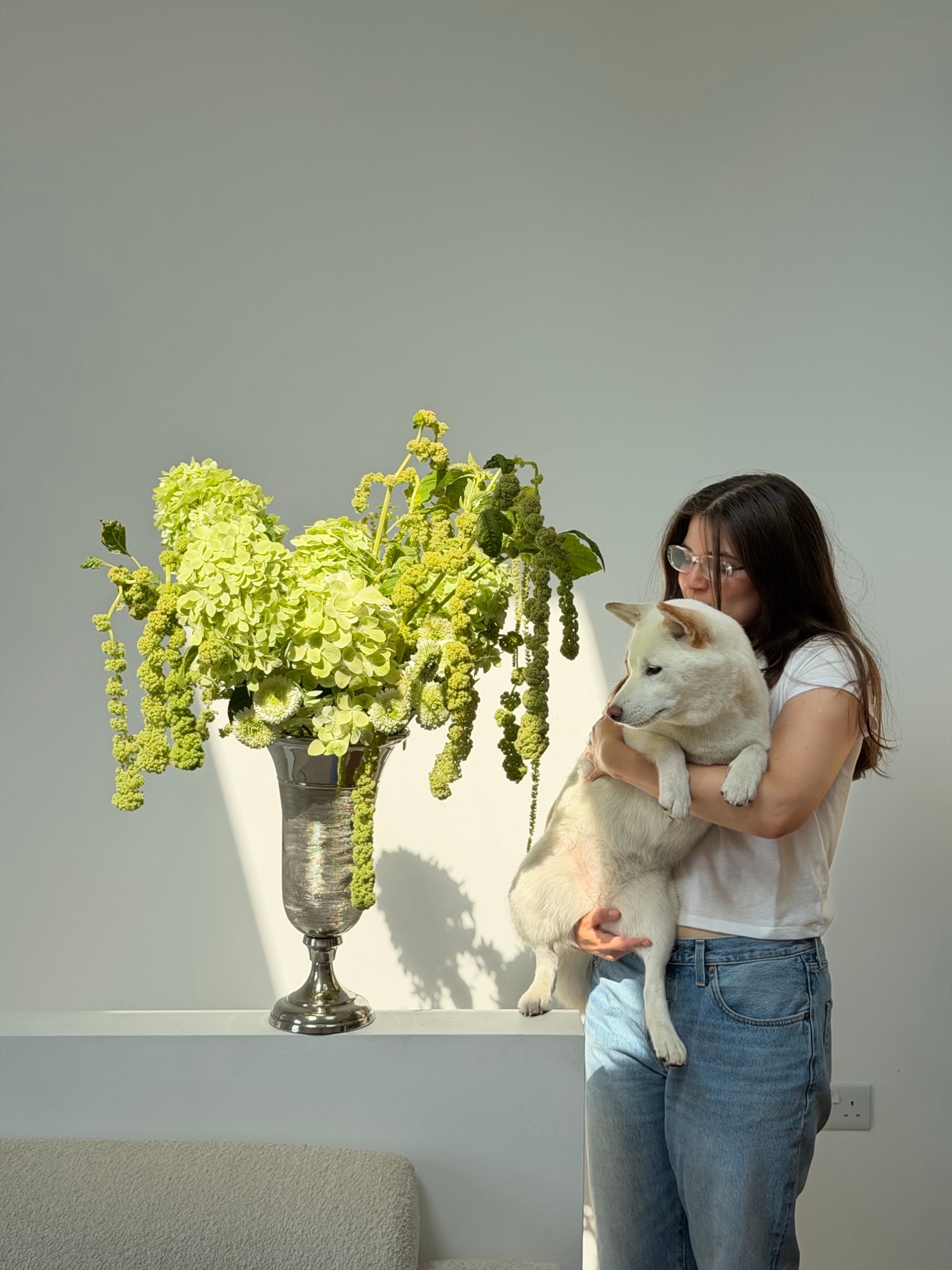 Founder holding a small white dog behind a tall lime-green floral arrangement