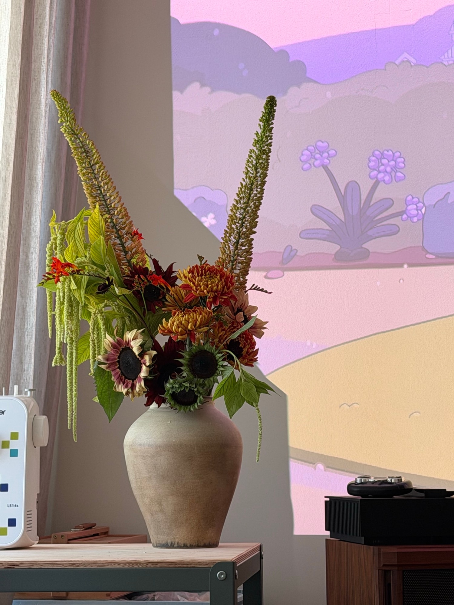 Burgundy sunflowers and long foxtail lily spires in a beige earthenware vase against a pastel wall projection