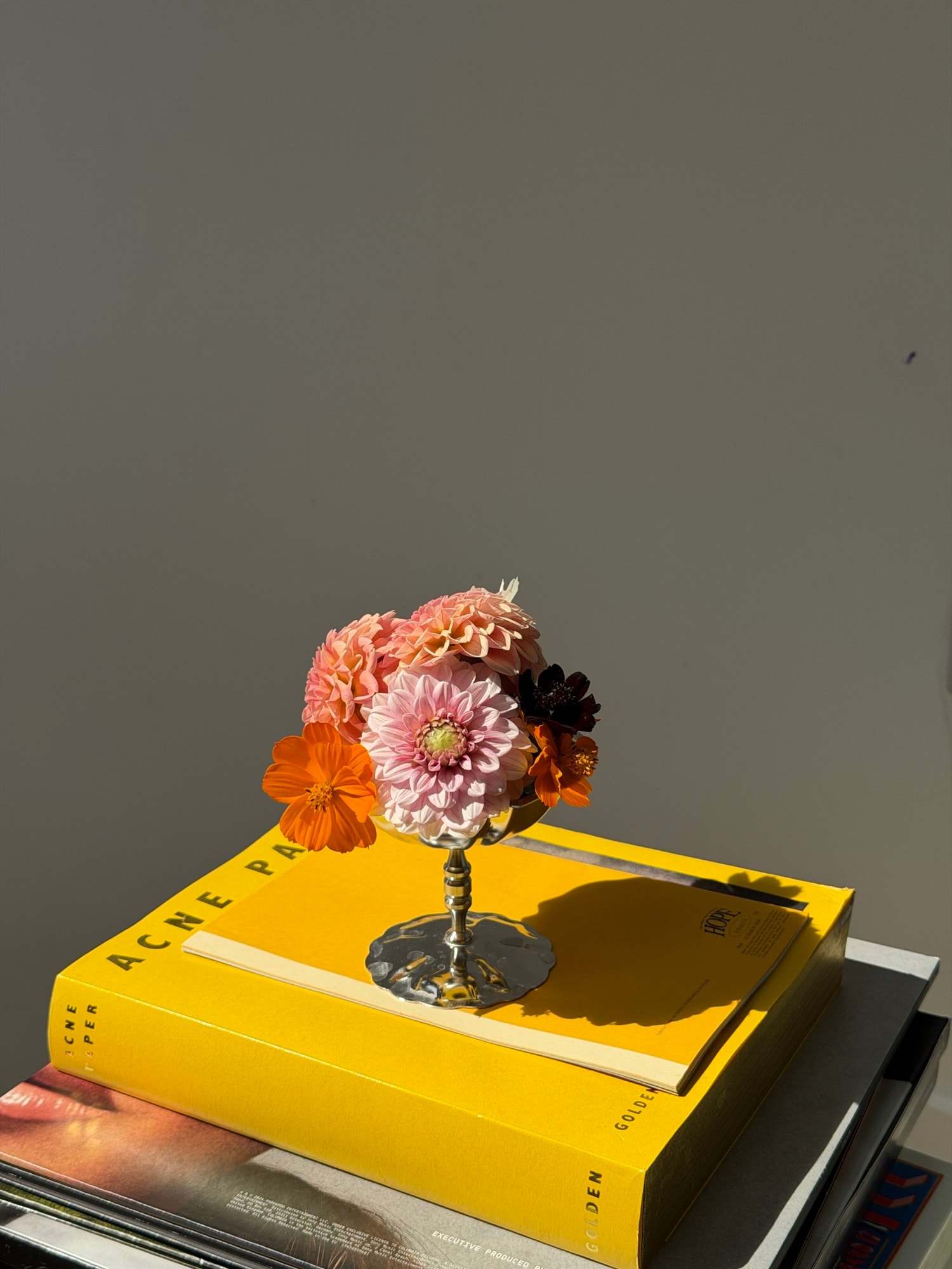 Top-down petite bouquet in silver pedestal vase on yellow book stack