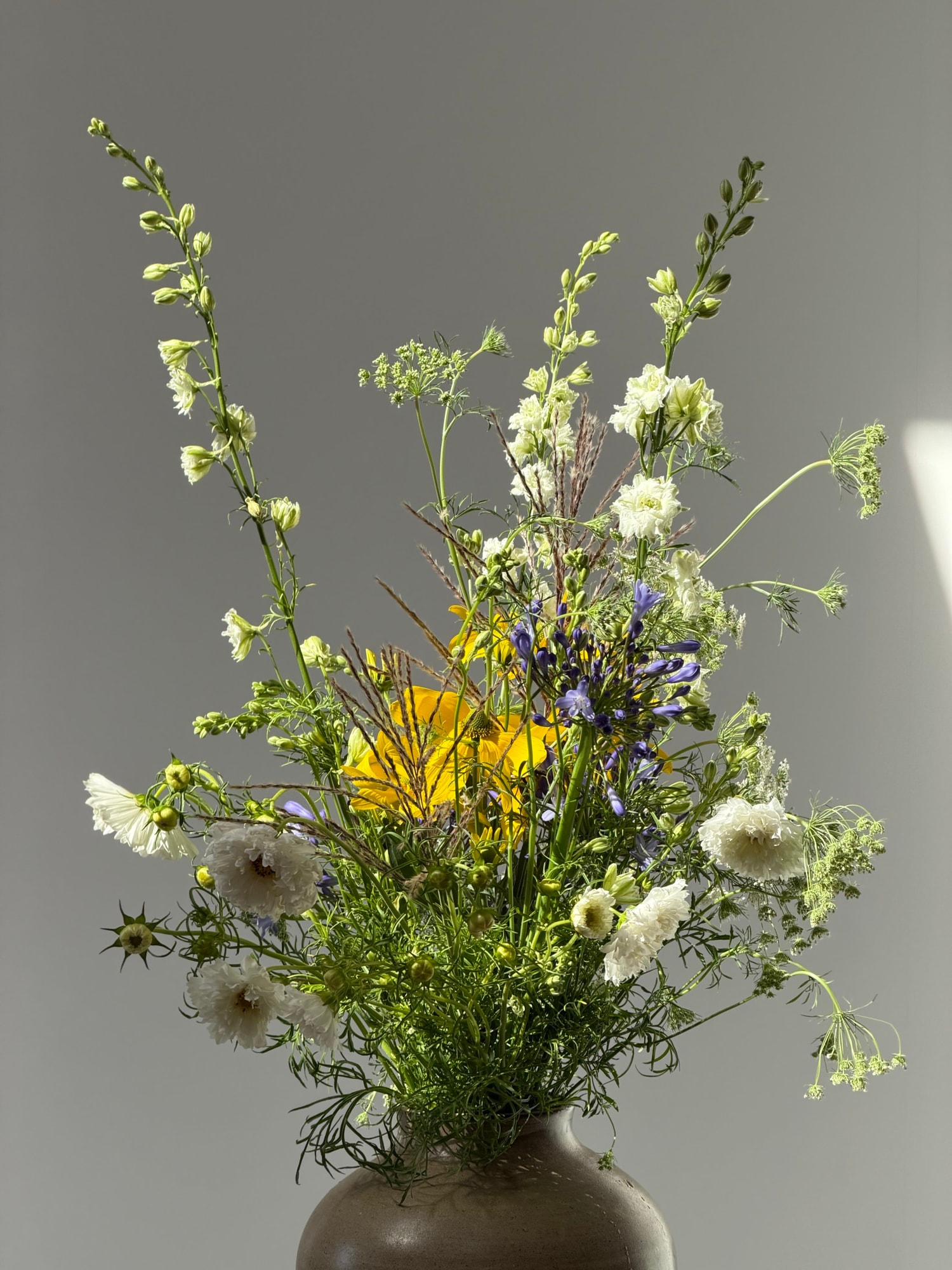 Airy wildflower arrangement spilling from a dark ceramic vase